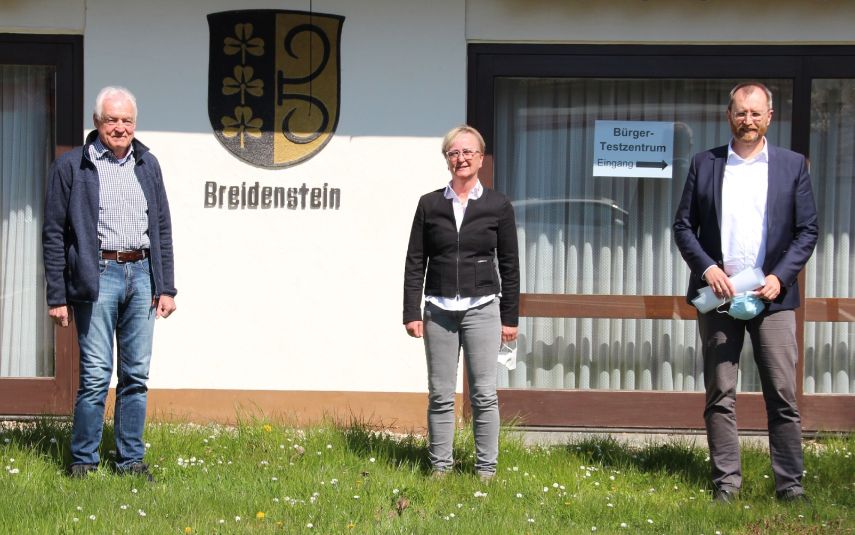 3 Gestalten vor einem Gebäude mit Stadtwappen "Breidenstein"