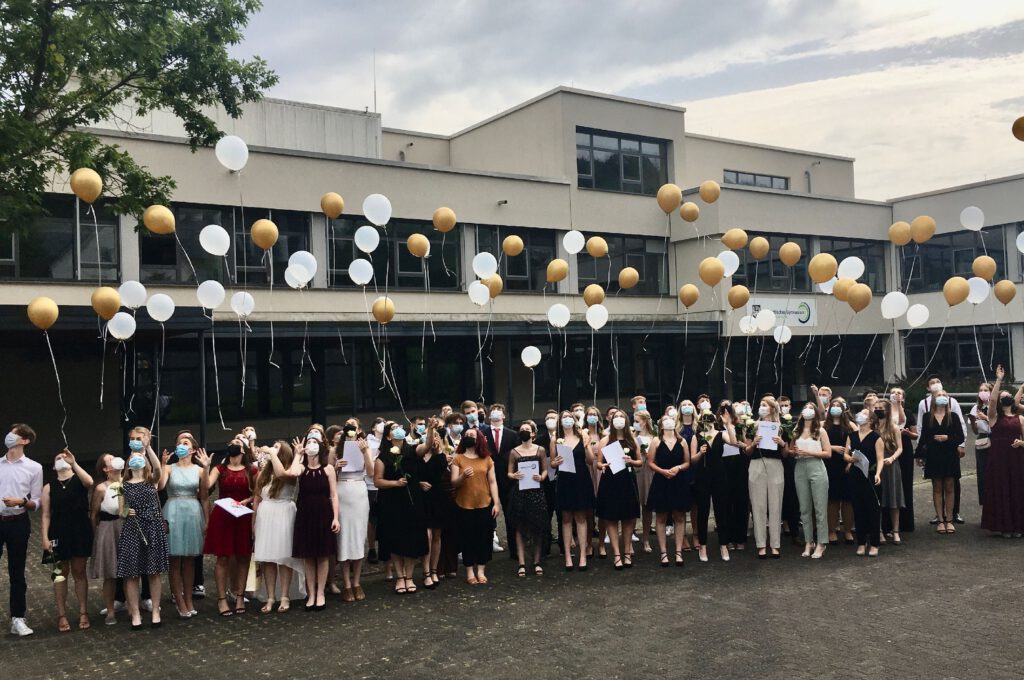großer Abiturientenjahrgang lässt weiße und goldfarbene Ballons steigen.