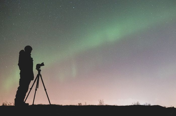 Schattenriss Mann vor Sternenhimmel und Polarlicht mit Kamera