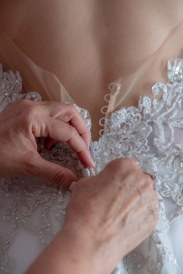 Mann knöpft Brautkleid zu. (Detailaufnahme)