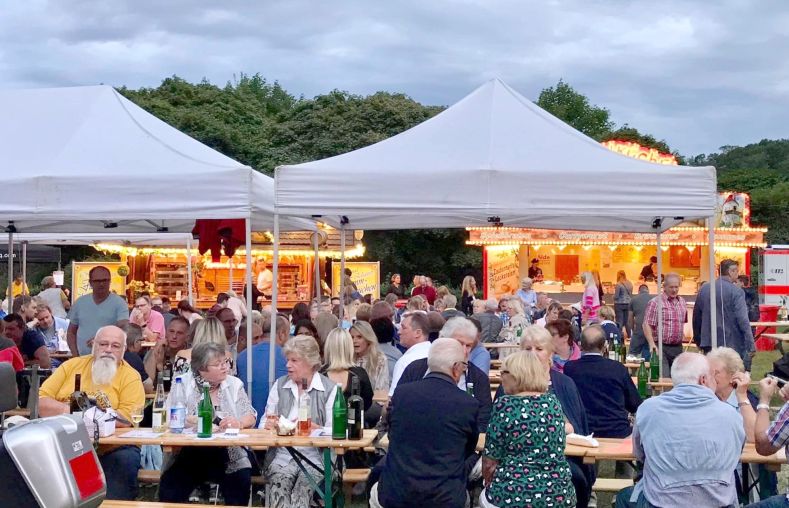 Leute feiern an Bierzeltgarnituren auf einer Wiese