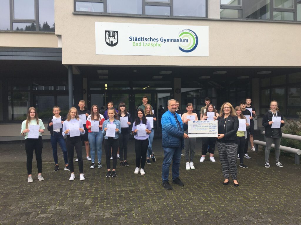 Lehrerin übergibt Scheck an Pfarrer. Schulklasse dahinter