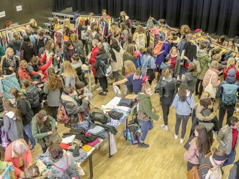überwiegend junge Frauen beim Kleidertauschen in einem großen Saal