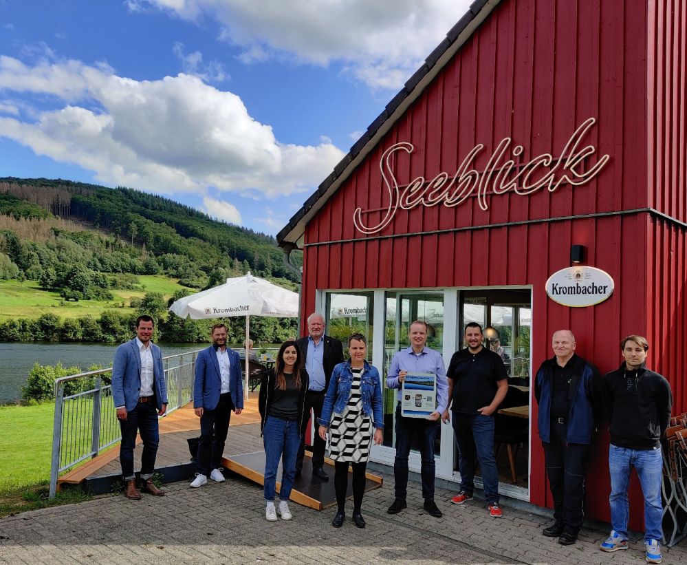 9 Leute stehen vor dem Restaurant Seeblick: Christian Salzmann (Krombacher Brauerei), Christoph Felkl (Bürgermeister Breidenbach), Tina
Hemmati (Leiterin des Gaststättenbetriebes), Jürgen Schneider (Erster Stadtrat Biedenkopf), Kirsten
Fründt (Landrätin Marburg-Biedenkopf), Mike-Oliver Klotz (Geschäftsführer Perfstausee-Betreiber
GmbH), Daniel Benken (Geschäftsführer lake house GmbH), Hartmut Klingelhöfer (Technischer
Betriebsleiter Wasserverband Oberes Lahngebiet), Pablo Ruhr (Geschäftsführer lake house GmbH)