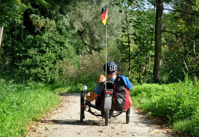 Mann fährt Liegerad auf einem Waldweg.
