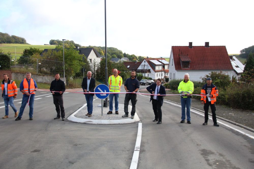 9 Leute schneiden symbolisch ein quer über die Fahrbahn gespanntes rot-weißes Band entzwei