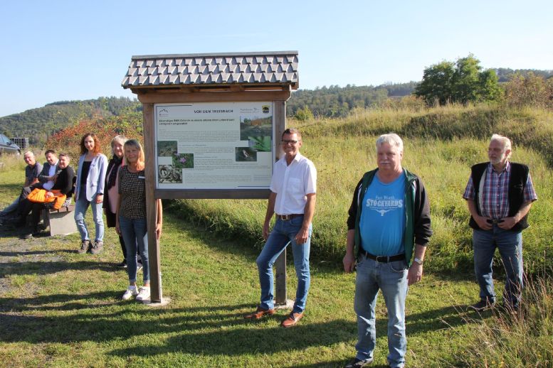 9 Leute stehen auf einer Wiese herum - im Vordergrund eine bebilderte Infotafel
