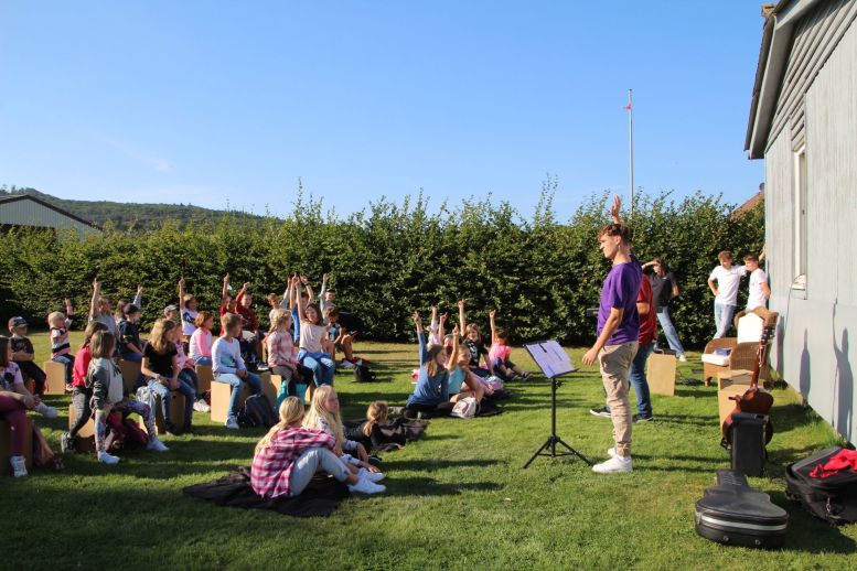 Kinder sitzen auf Hockern auf einer Wiese und machen Bewegungen