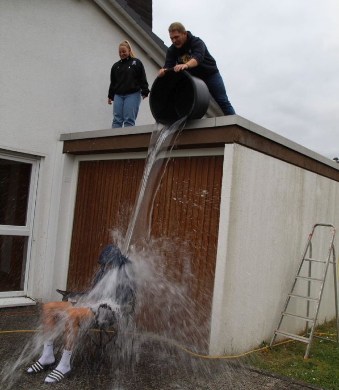 2 Leute schütten einen Eimer Wasser vom Dach aus auf einen Sitzenden