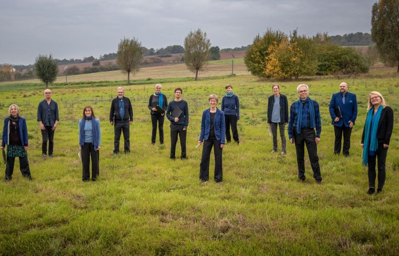 12 Musikerinnen und Musiker in schwarz-blauen Outfits auf einer Wiese