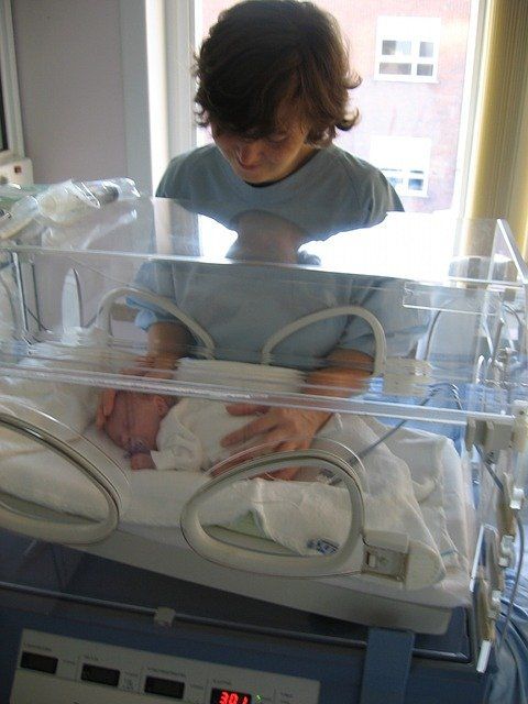 Baby im Inkubator. Frau im Kittel streichelt es