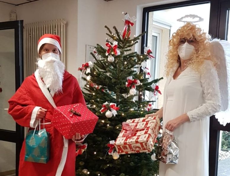 Nikolaus und ein Engelein stehen vor einem Weihnachtsbaum und halten Geschenke