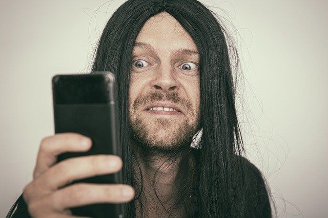 versiffter User mit Bart und langen Haaren am Handy