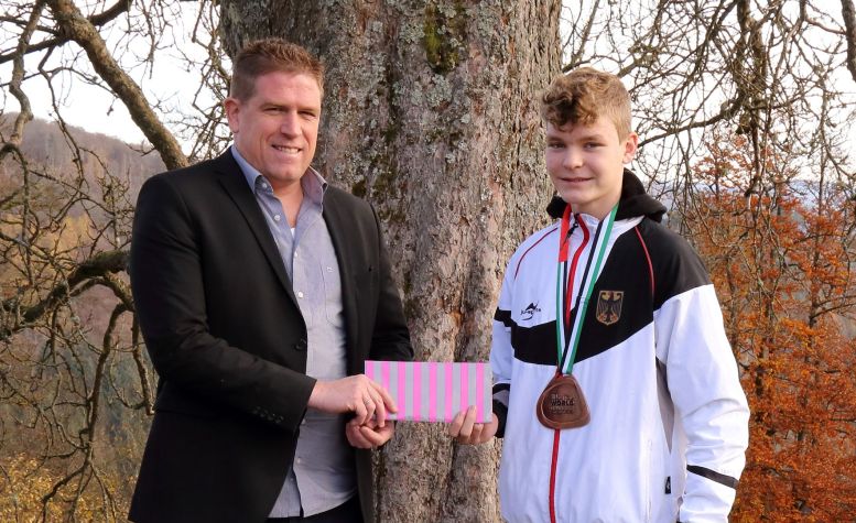 Schulleiter gratuliert Jungen im Sportoutfit und mit Medaille um den Hals