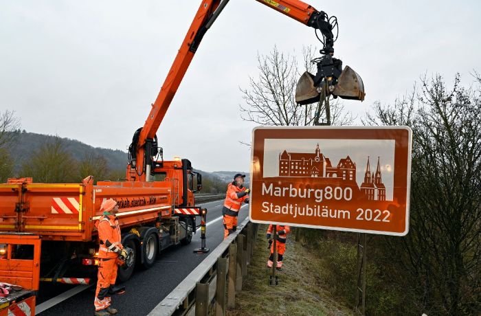 Kran auf der Straße. e Mitarbeiter stellen ein großes Schild auf