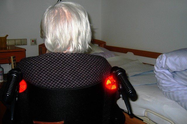 Frau im Rollstuhl vor Pflegebett