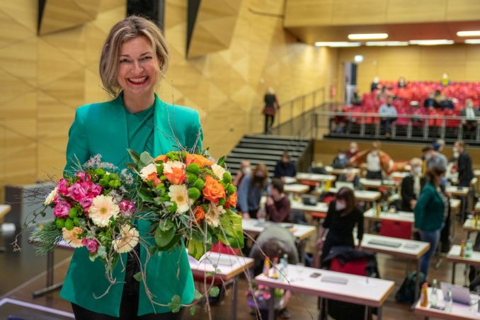 Ältere Frau mit 2 Blumensträußen lacht in die Kamera
