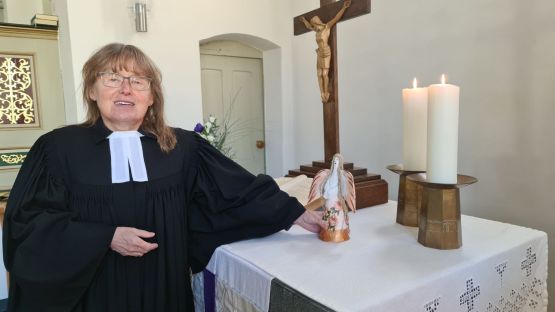 Ältere, verhärmte und unsympathisch wirkende Frau mit Brille und schlechter Frisur im Talar