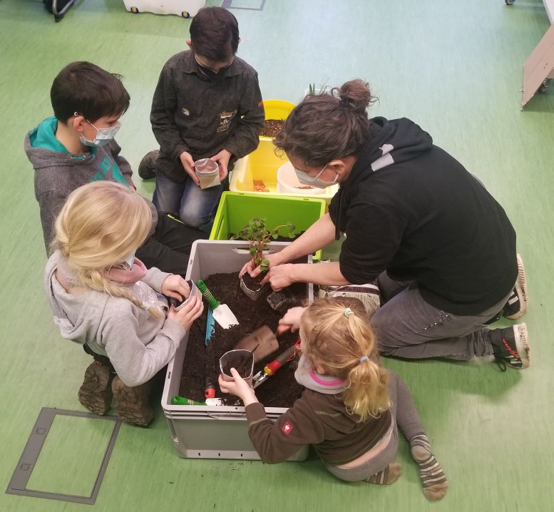 4 Kinder und eine Leiterin füllen Erde in Pflanztöpfe