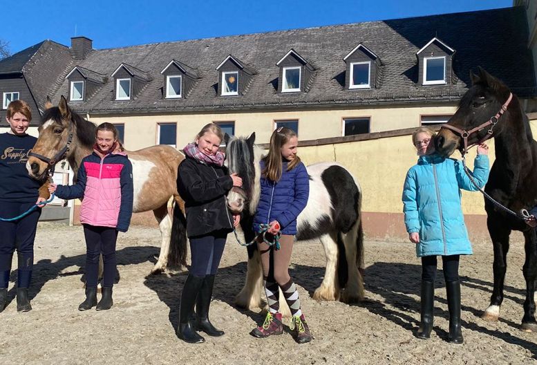 Ein Junge und vier Mädels mit Pferden vor dem Schulgebäude