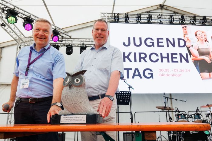 2 Männer auf dem Podium und eine Eule aus Stein.